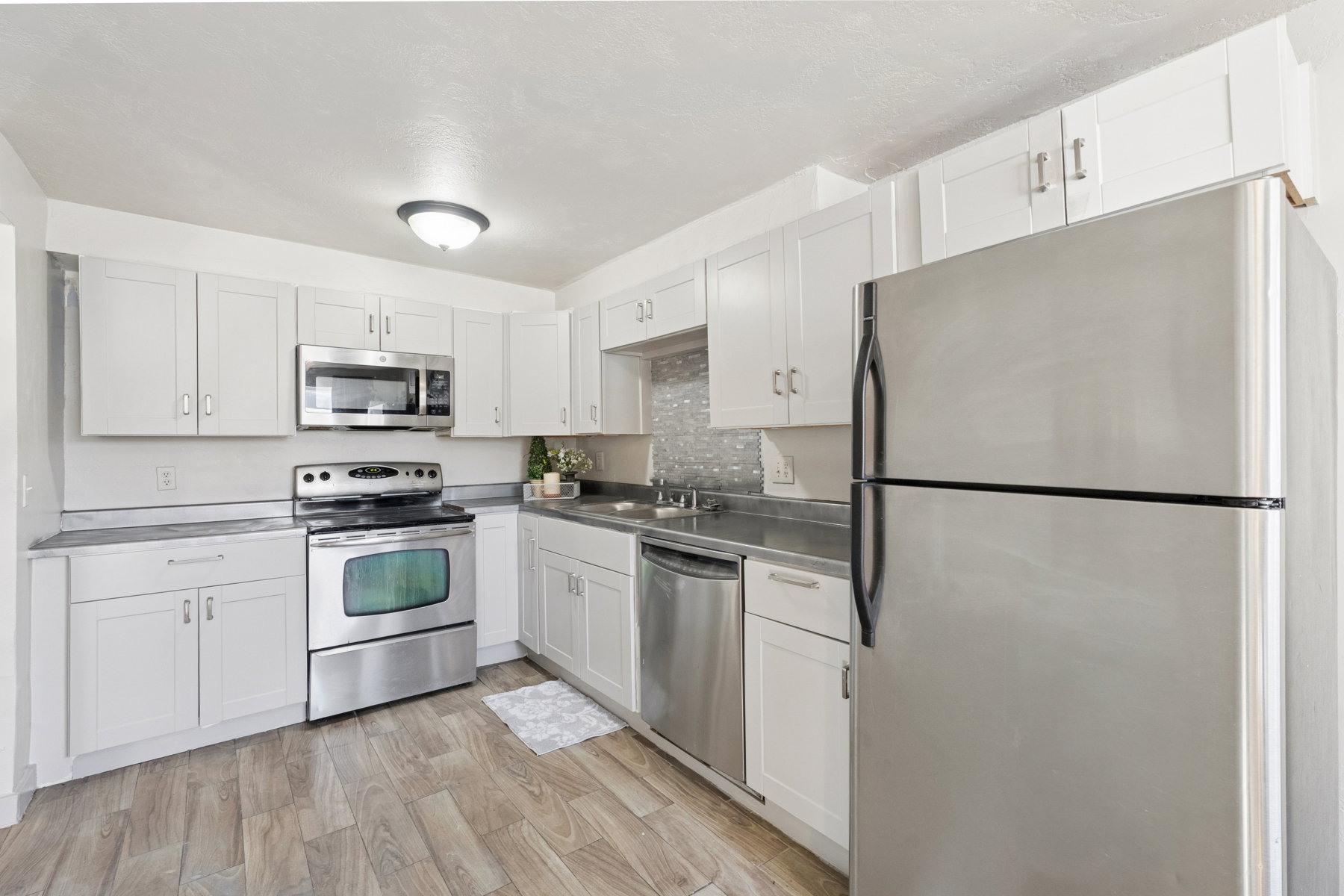 Kitchen featuring white shaker cabinetry, stainless steel appliances, grey countertops, a tiled backsplash, and wood-finish flooring