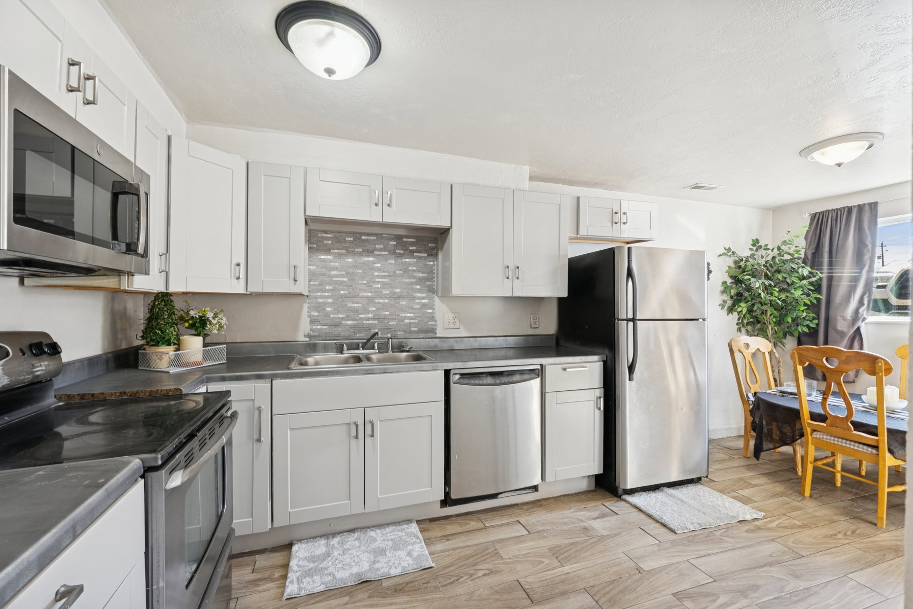 Updated kitchen featuring white shaker cabinetry, stainless steel appliances, a mosaic tile backsplash, dark countertops, and wood-finish flooring