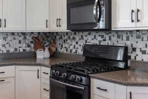 Kitchen featuring a black gas range, coordinating black microwave, speckled countertops, and white shaker-style cabinetry with matte black hardware