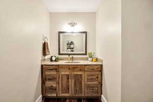 Wood-finish vanity with a single basin, stone countertop, and an overhead vanity light