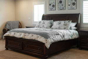 Spacious primary bedroom featuring light neutral wall tones, carpet flooring, and white plantation shutters