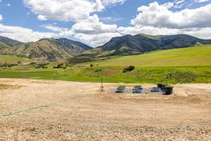 Expansive open lot featuring a gravel surface, established vegetation, and a mountainous backdrop