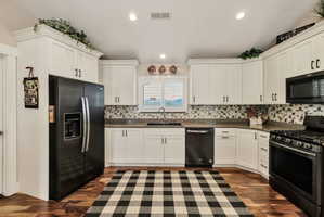 Bright kitchen featuring white shaker cabinetry, dark countertops, a mosaic tile backsplash, black appliances, and wood-finish flooring