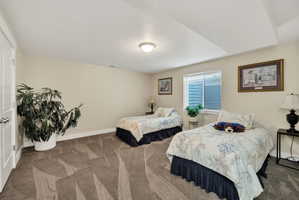Spacious bedroom featuring light neutral walls, patterned carpet flooring, a single window with blinds, and a white paneled door