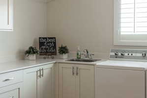 Laundry area featuring white cabinetry, light-toned countertops, a stainless steel sink with a chrome faucet, and a window with white plantation shutters