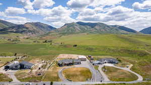 Expansive property featuring a modern ranch-style residence, a circular driveway, an attached multi-car garage, and a detached outbuilding, all set against a backdrop of rolling green hills and distant mountains