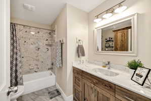 Bathroom featuring a wood-finish vanity with a white countertop and integrated sink, a white-framed mirror, and a three-light vanity fixture