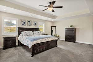 Spacious bedroom featuring neutral wall tones, tray ceiling, and ceiling fan with integrated lighting