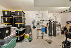 Utility room featuring a water softener system, water heater, and various plumbing installations