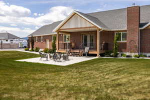 Expansive backyard featuring a large concrete patio, covered deck with wood-finish railing, and brick exterior