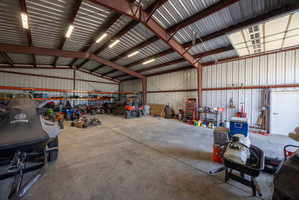 Spacious metal building featuring an open floor plan, concrete flooring, corrugated metal walls, exposed steel beams, and strip lighting fixtures