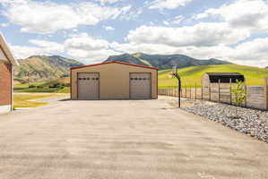 Spacious asphalt driveway fronting a large two-bay metal outbuilding with overhead doors