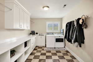 Spacious utility room featuring white cabinetry, extensive counter space, checkerboard flooring, a dedicated sink, and a window with plantation shutters