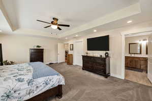 Spacious primary bedroom featuring a tray ceiling with a ceiling fan, recessed lighting, and soft carpet flooring