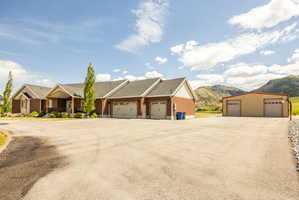 Brick exterior home with an attached multi-car garage, expansive paved driveway, and an additional detached two-bay structure, all set against a mountainous backdrop