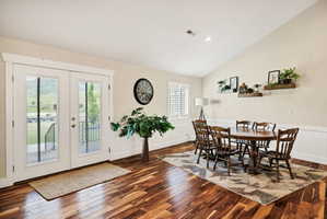 Vaulted ceiling dining area featuring wood-finish flooring, white wainscoting, and French doors opening to an exterior deck