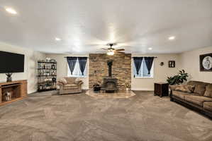 Spacious room featuring a stone-clad fireplace with a wood-burning stove, two windows, recessed lighting, and a ceiling fan