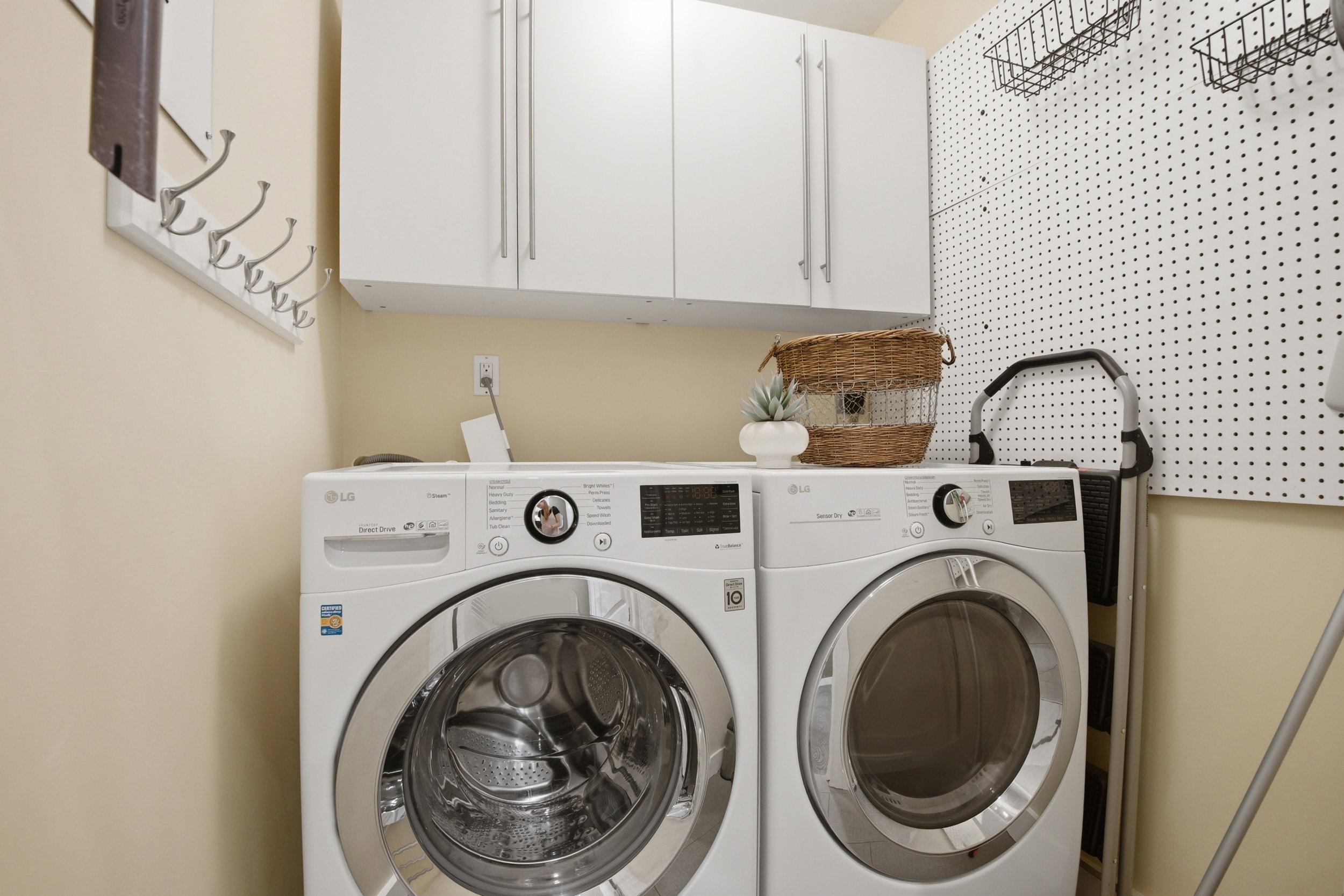Laundry area featuring upper white cabinetry, a white pegboard wall, and light neutral wall paint