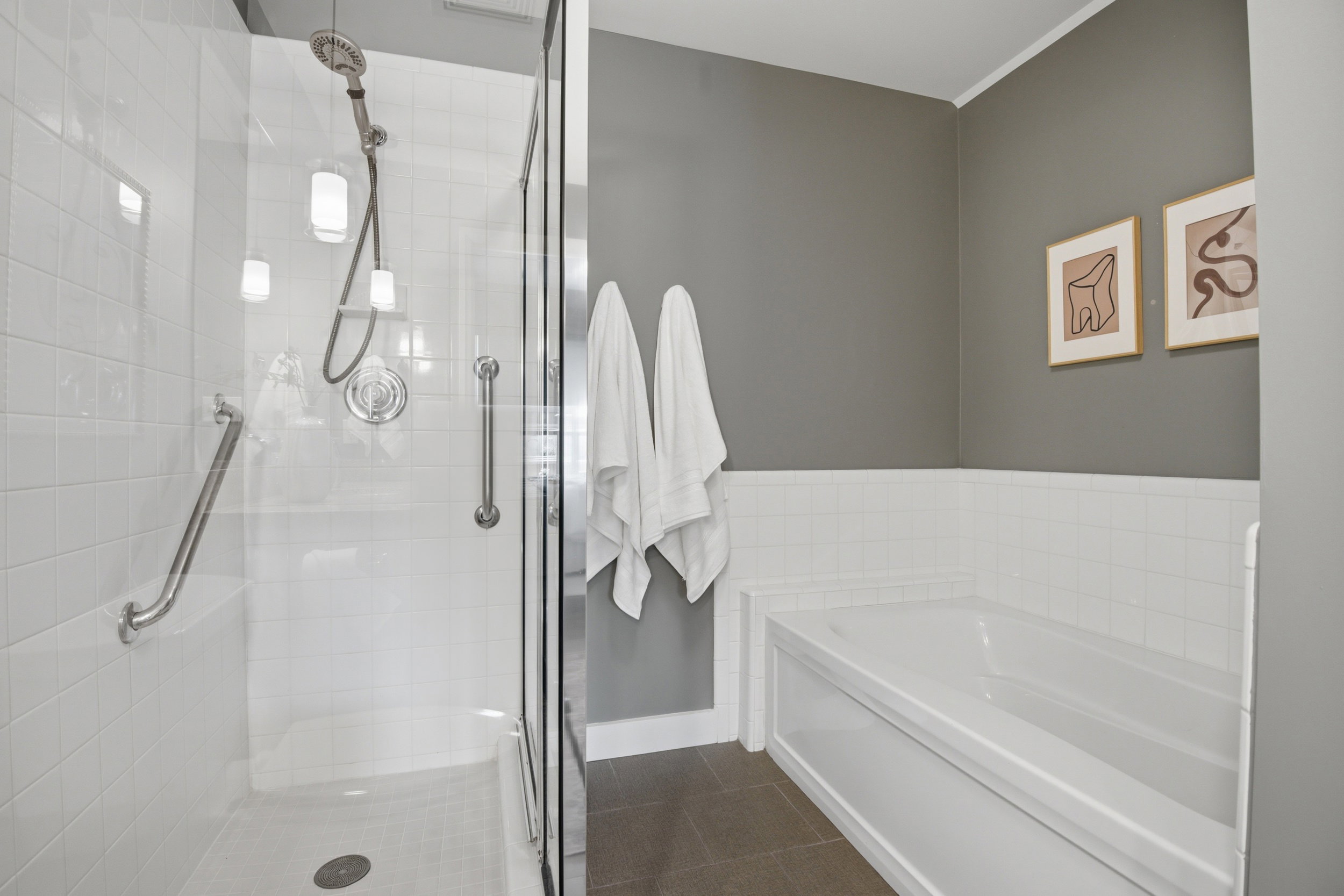 Bathroom featuring a glass-enclosed shower with white subway tile, an integrated shower bench, and grab bars