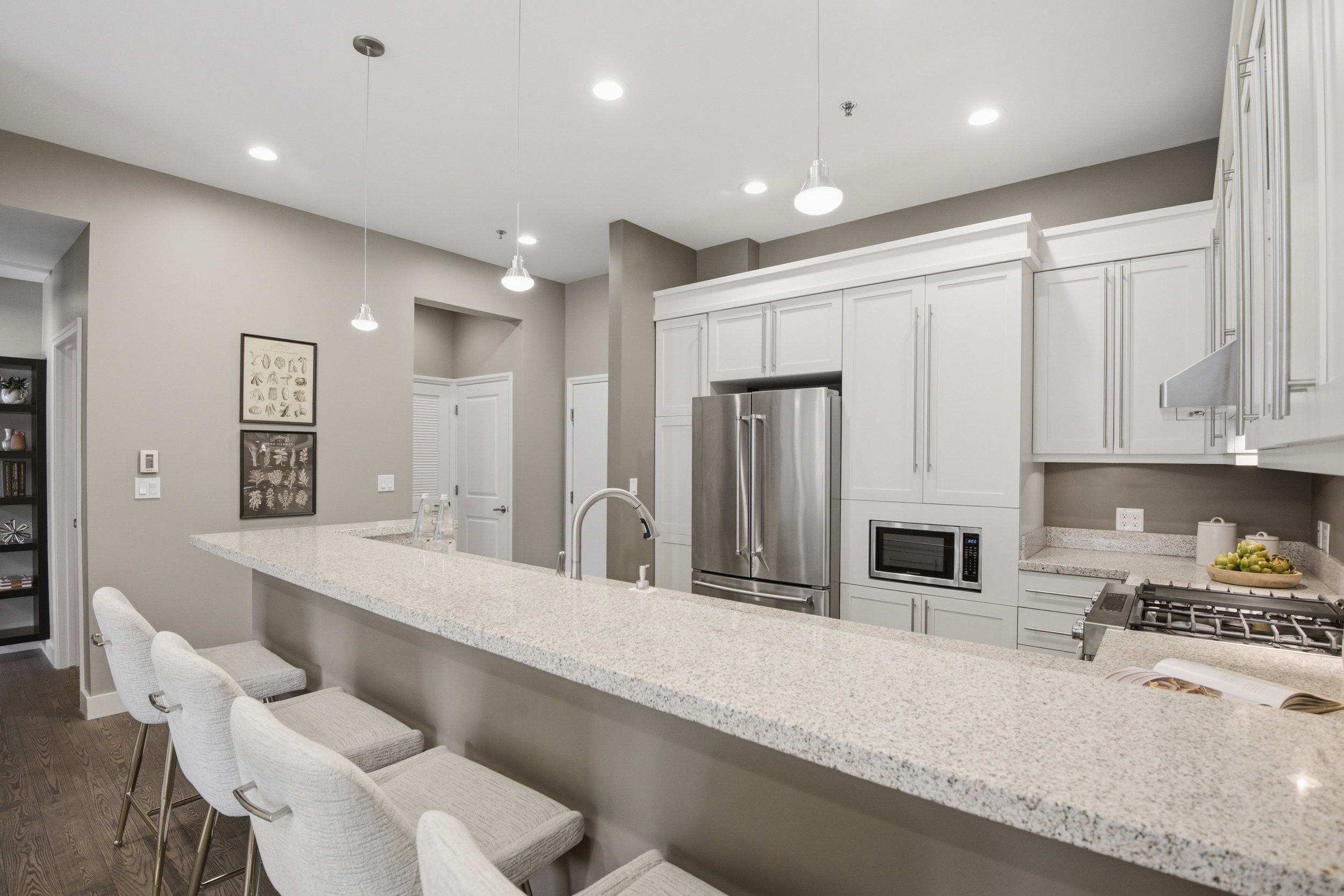 Kitchen featuring a large breakfast bar with light-colored countertop, stainless steel appliances, white cabinetry with crown molding, recessed lighting, and pendant lighting fixtures