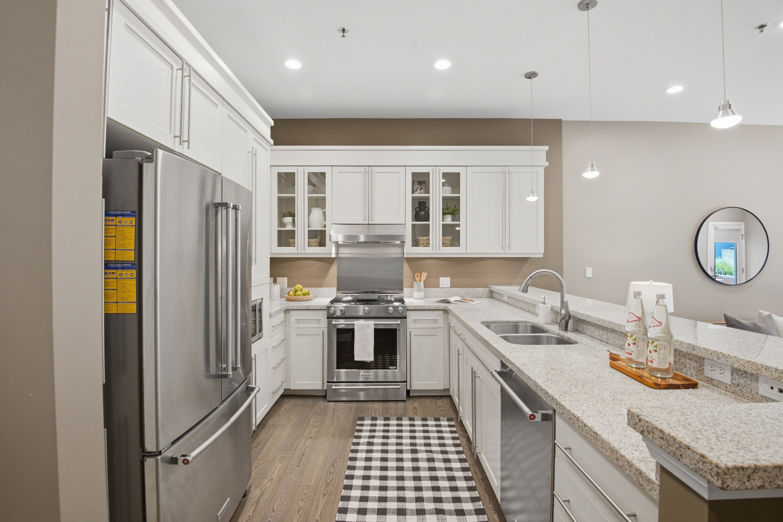 Well-appointed kitchen featuring a stainless steel appliance suite, white shaker cabinetry, stone-finish countertops, wood-finish flooring, and recessed lighting