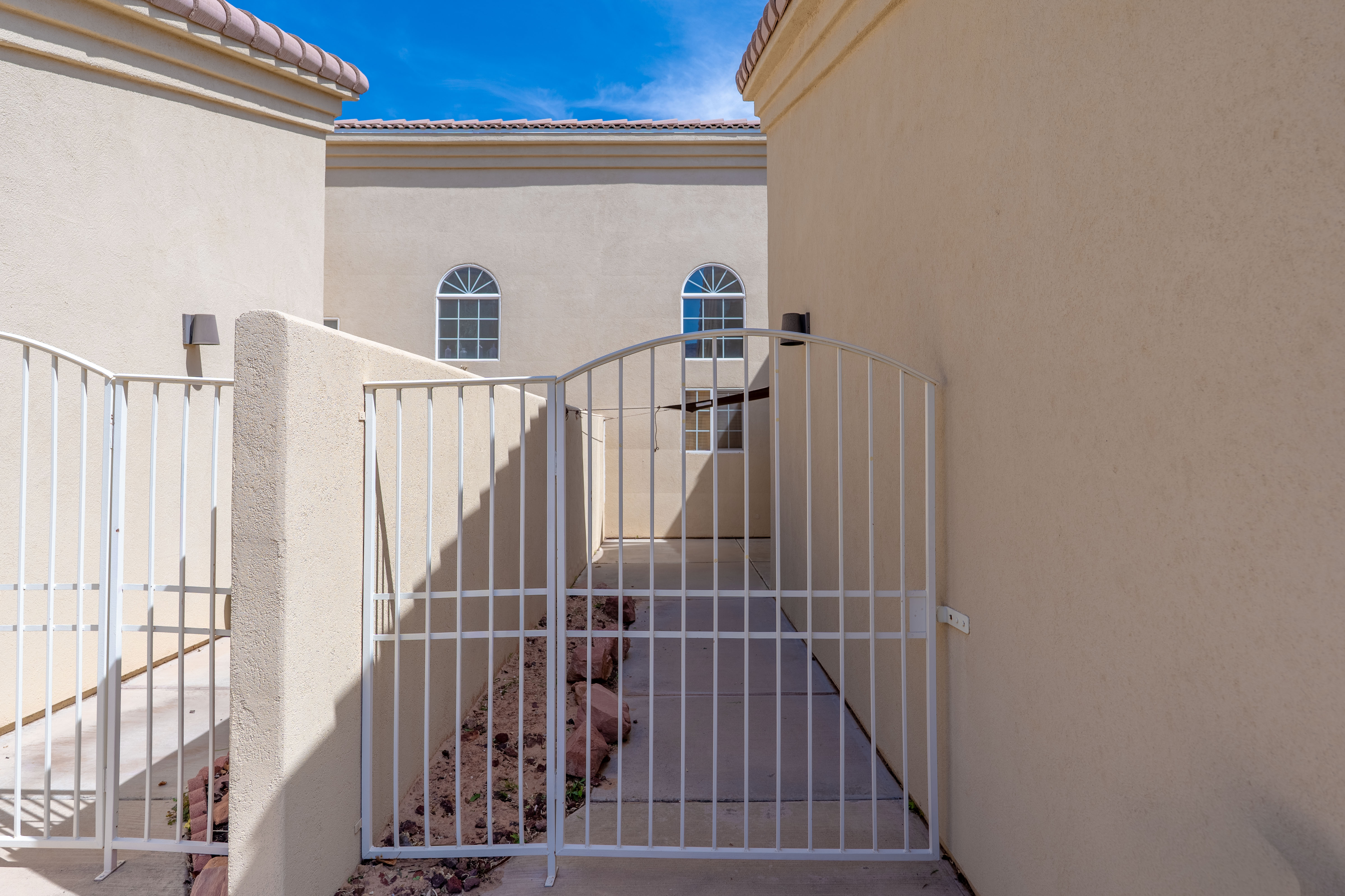 Arched white metal gate providing access to a concrete pathway