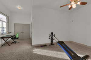Carpeted interior space featuring a large window, double doors, a flush-mount ceiling light, and a ceiling fan with integrated lighting