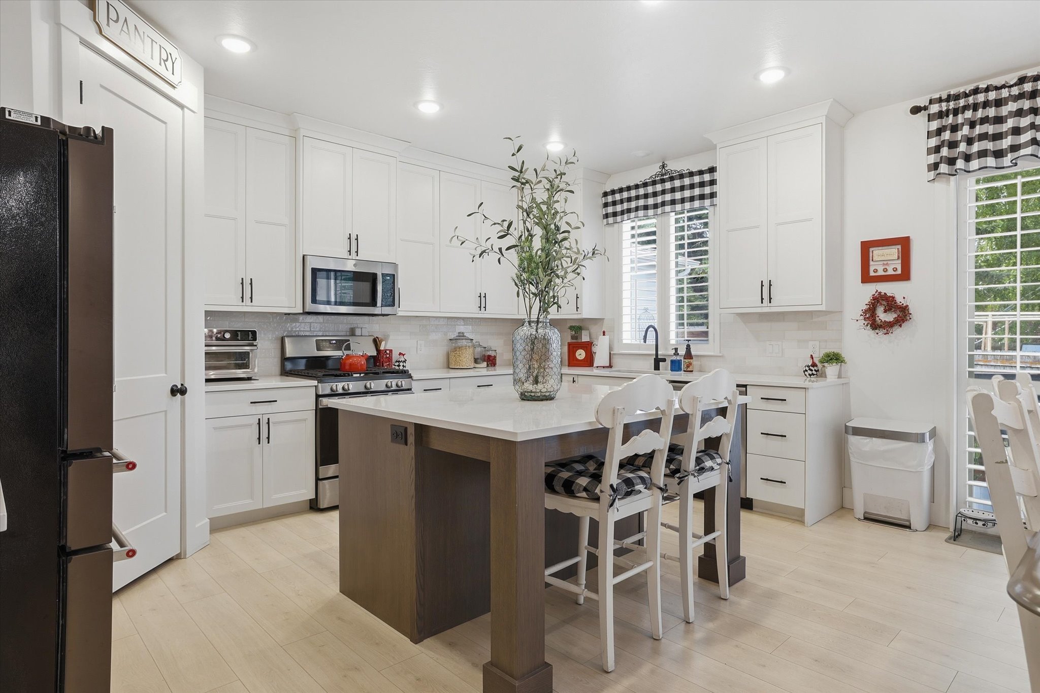 Kitchen featuring white shaker cabinetry, stainless steel appliances, a center island with bar seating, light wood-finish flooring, and a pantry door