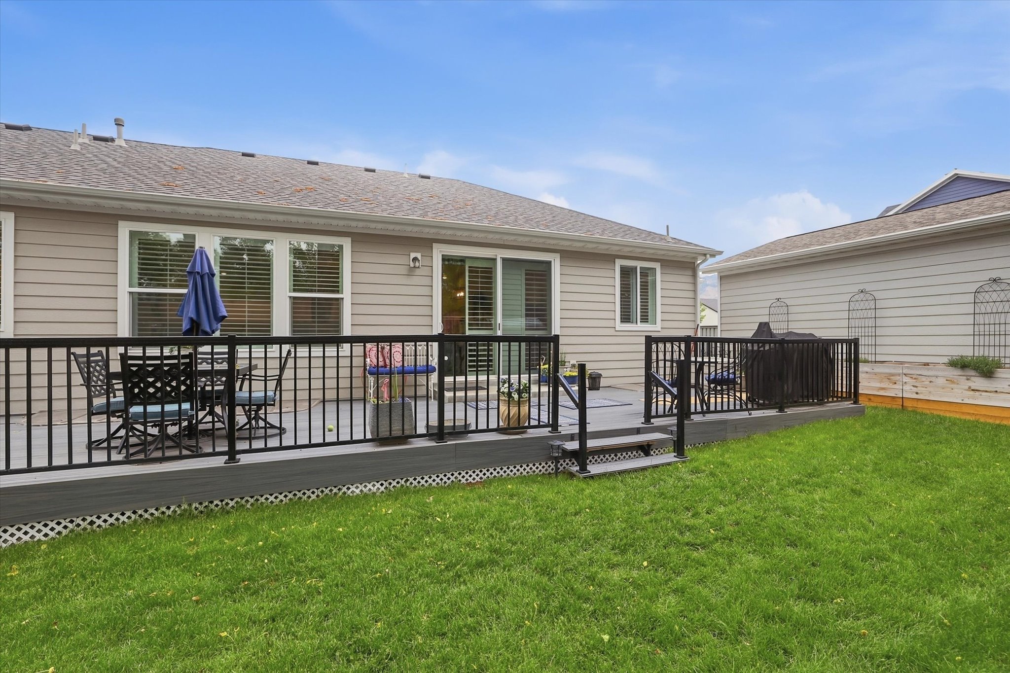 Rear exterior featuring a grey composite deck with black railings, a sliding glass door, multiple large windows with blinds, and a green lawn