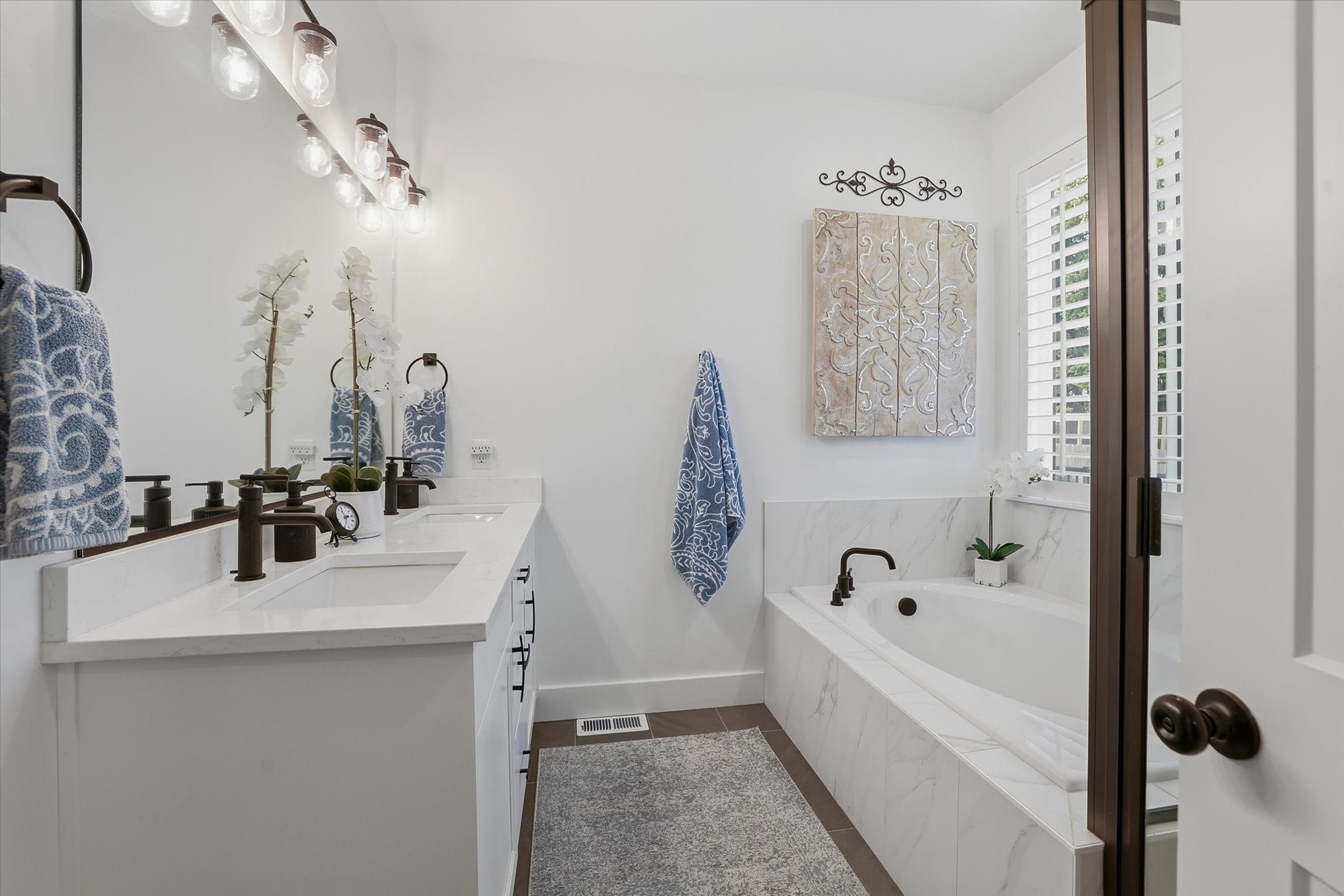 Bathroom featuring a double vanity with white cabinetry and quartz countertops, dual undermount sinks, and bronze-finish fixtures