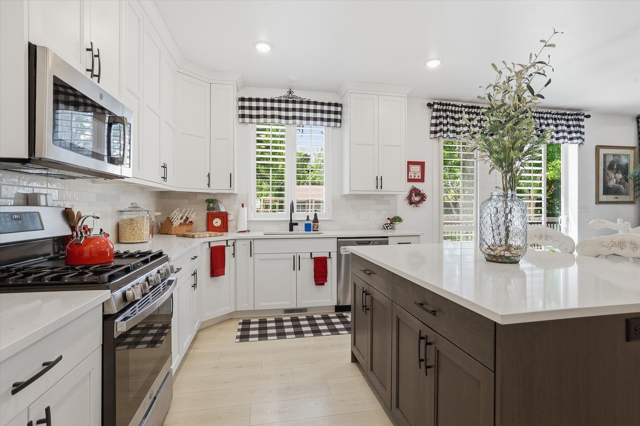 Modern kitchen featuring white shaker cabinetry, stainless steel appliances, a center island with a light-toned countertop, light wood-finish flooring, and a subway tile backsplash
