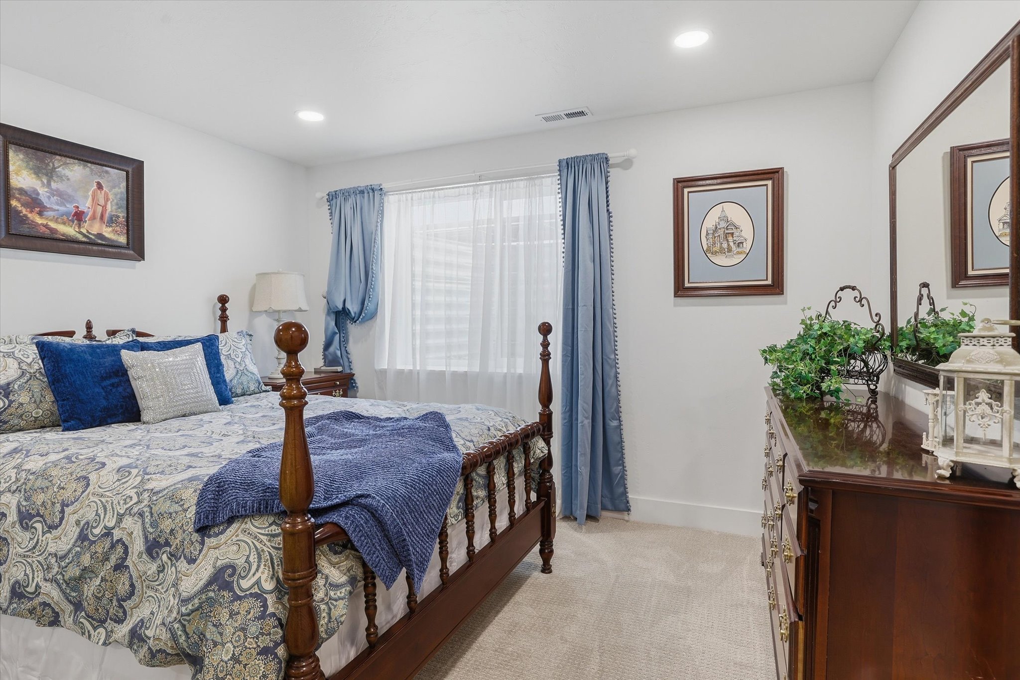 Carpeted bedroom featuring recessed lighting, a window with sheer and blue drapes, and a dark wood dresser with an attached mirror