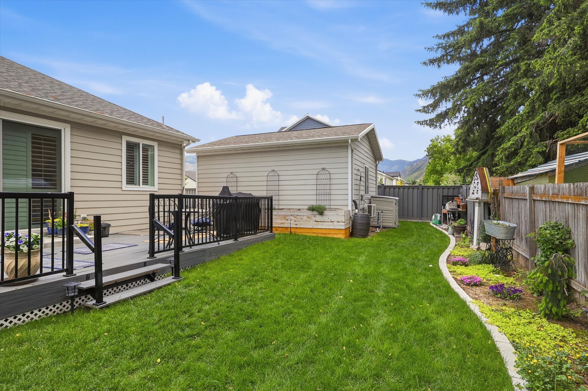 Expansive backyard featuring a composite deck with black metal railings, a manicured lawn, and a landscaped garden bed