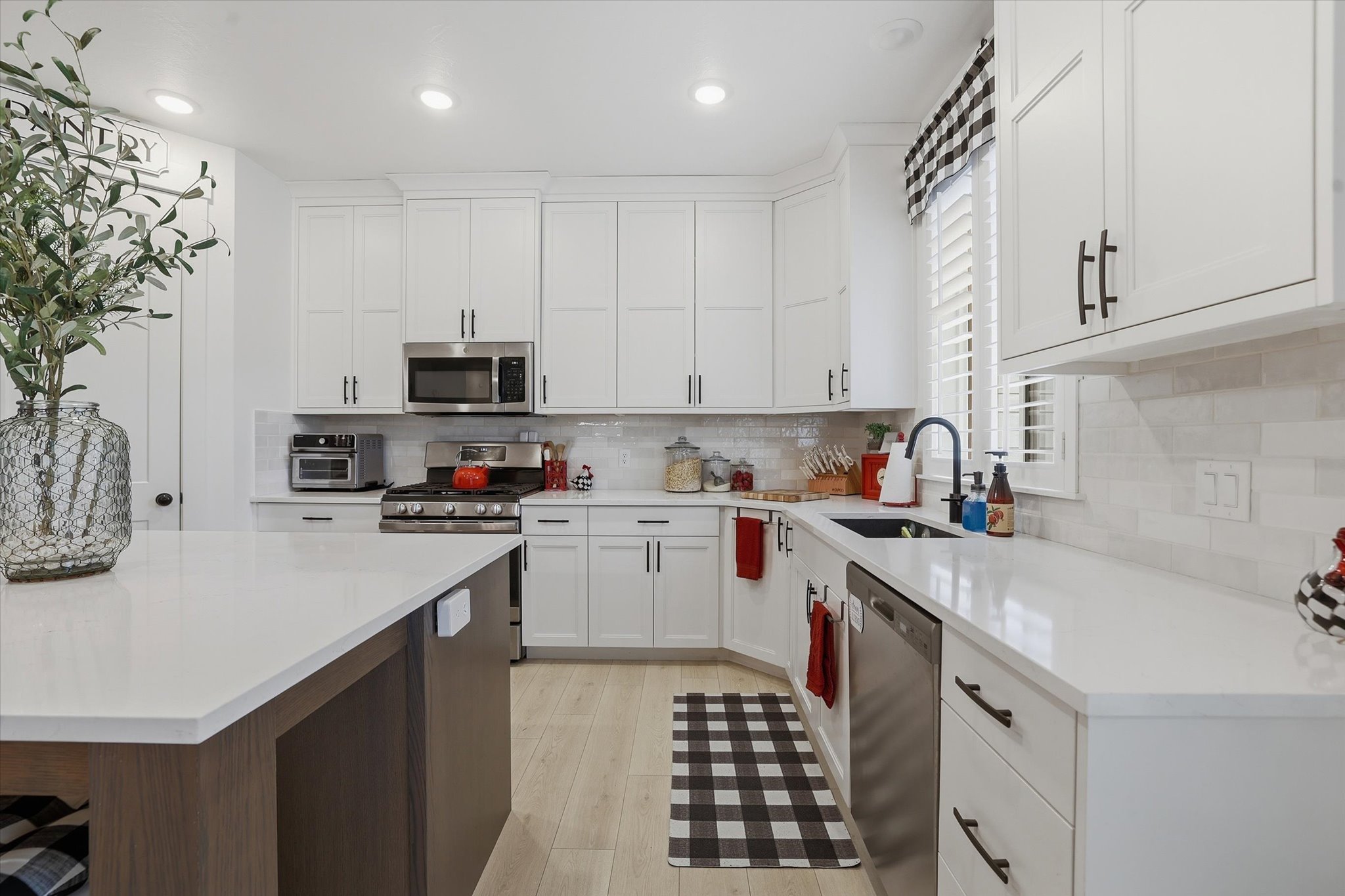 Kitchen featuring white shaker cabinetry, stainless steel appliances, a center island with a light countertop, white subway tile backsplash, and wood-finish flooring