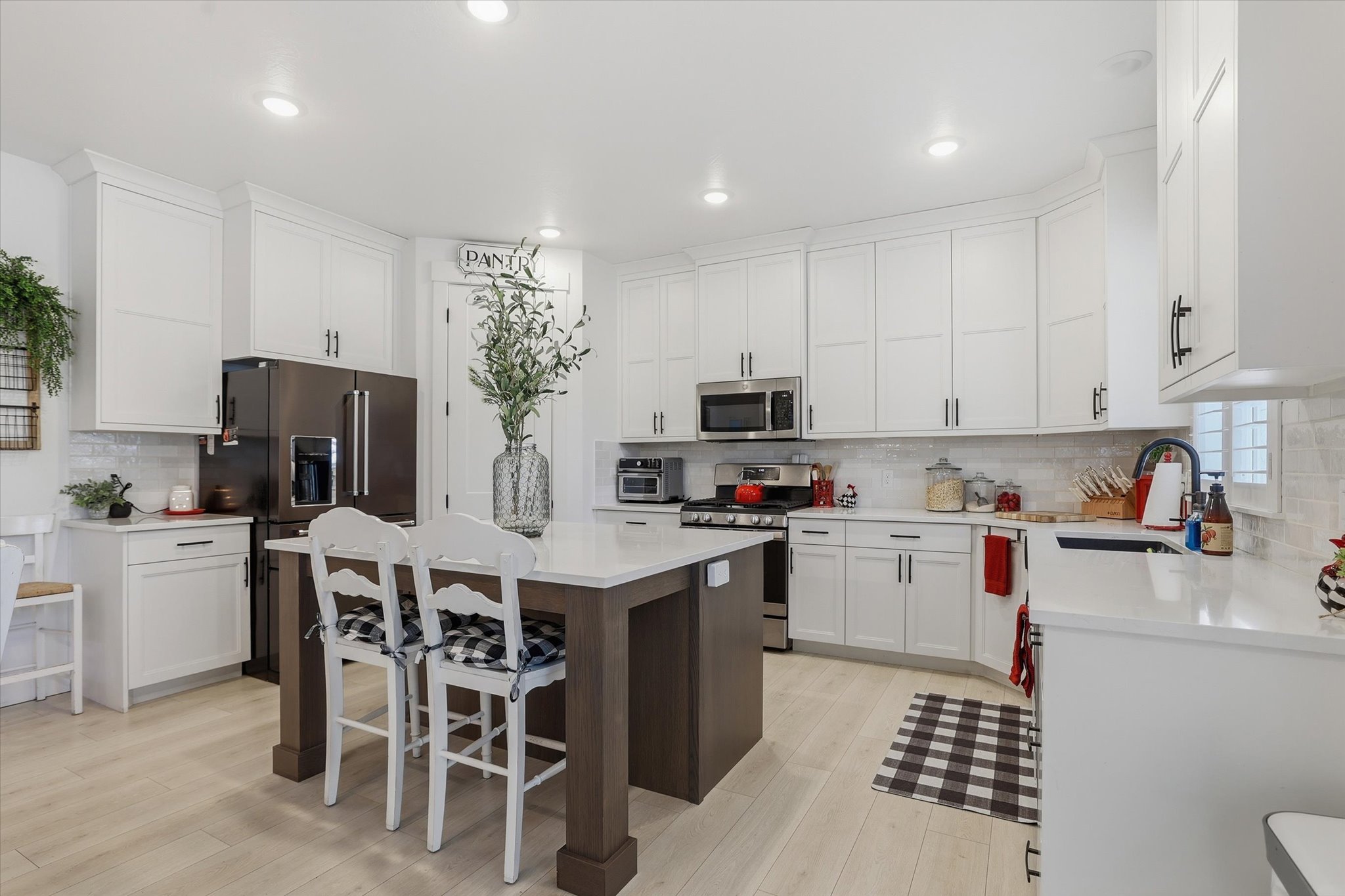 Bright kitchen featuring abundant white shaker cabinetry, light wood-finish flooring, a central island with countertop seating, stainless steel appliances, and a tiled backsplash