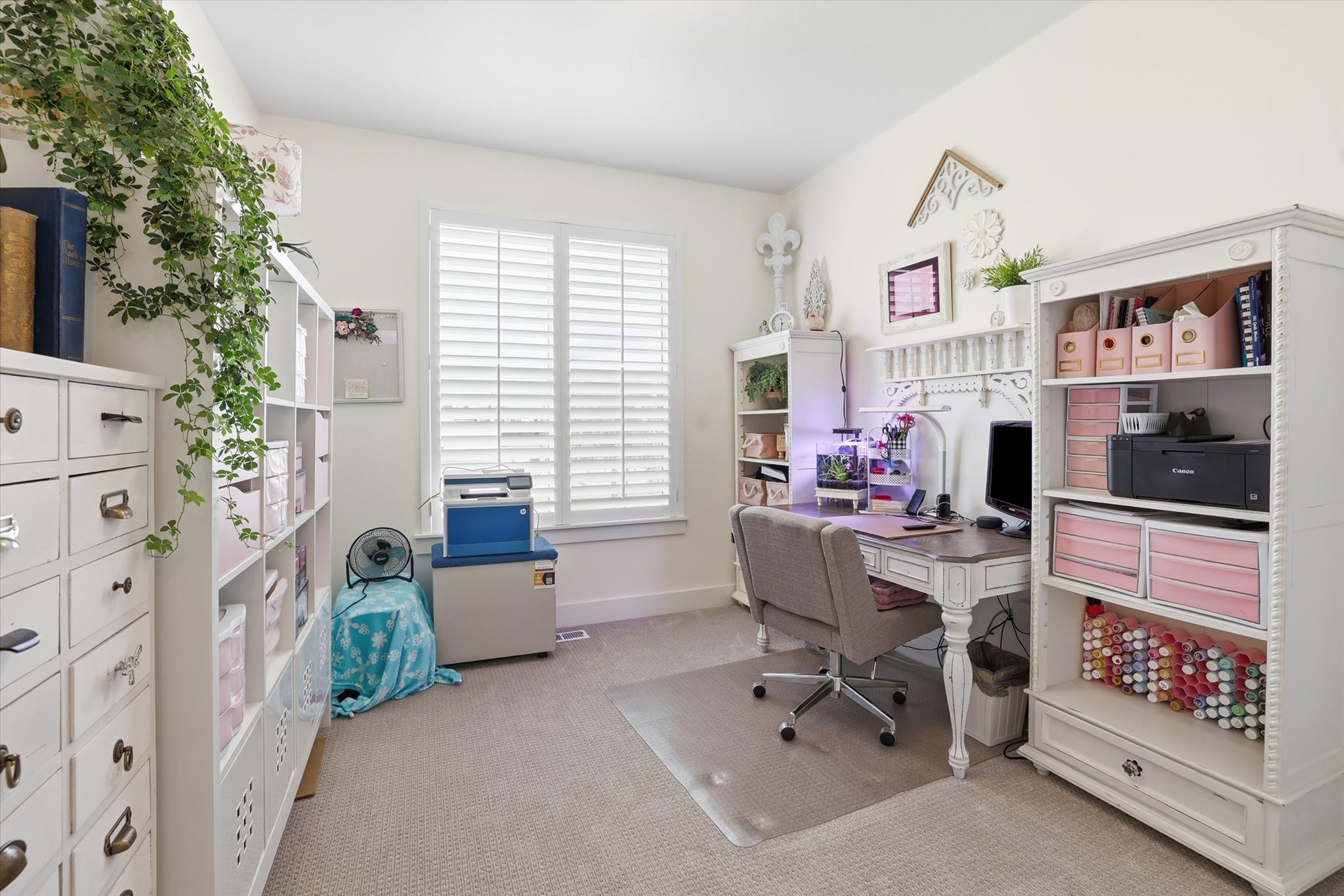 Bright room featuring a window with white plantation shutters, neutral carpeting, and white built-in shelving units