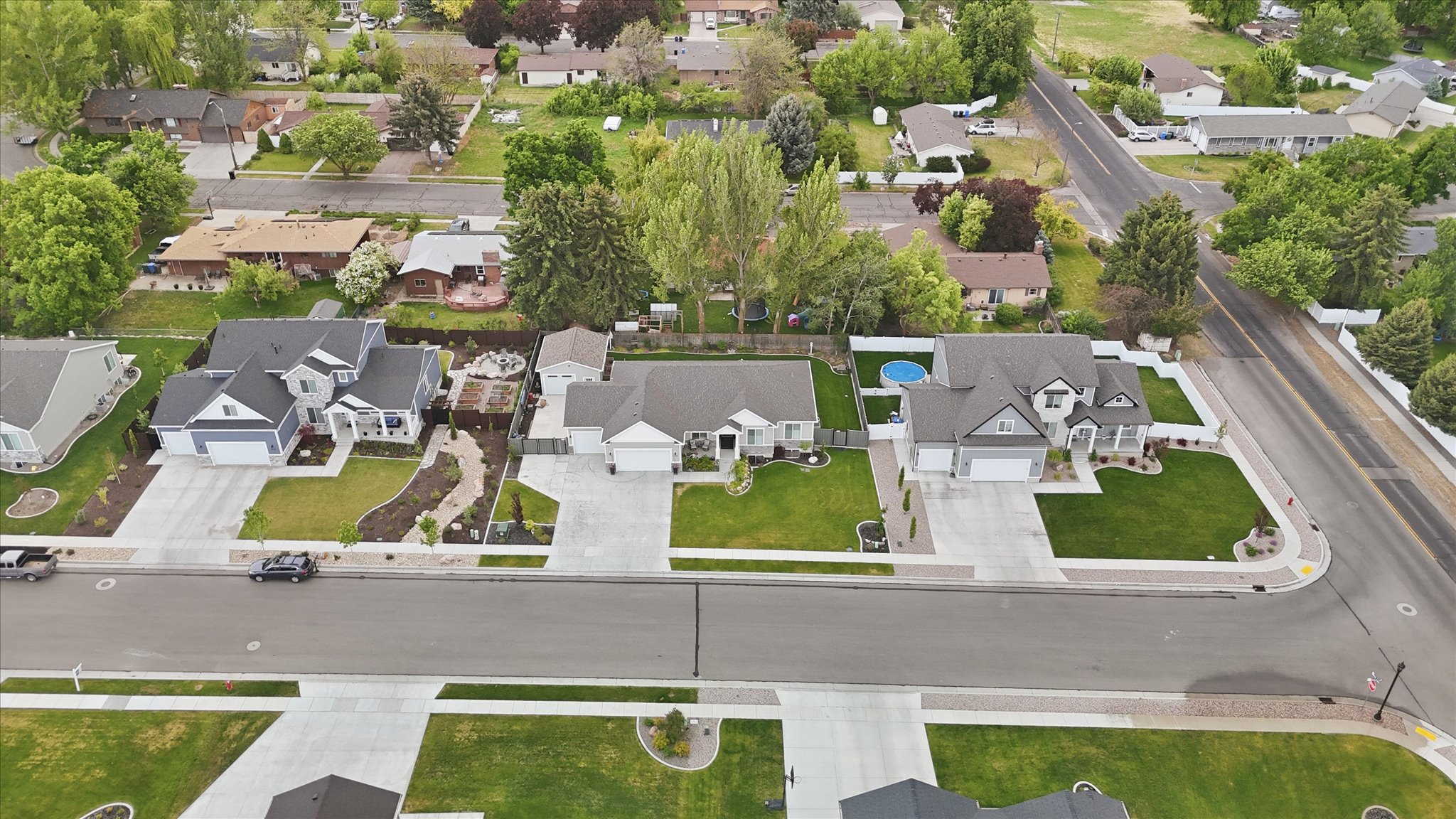 Residential street featuring three distinct homes with manicured lawns, concrete driveways, and surrounding green spaces
