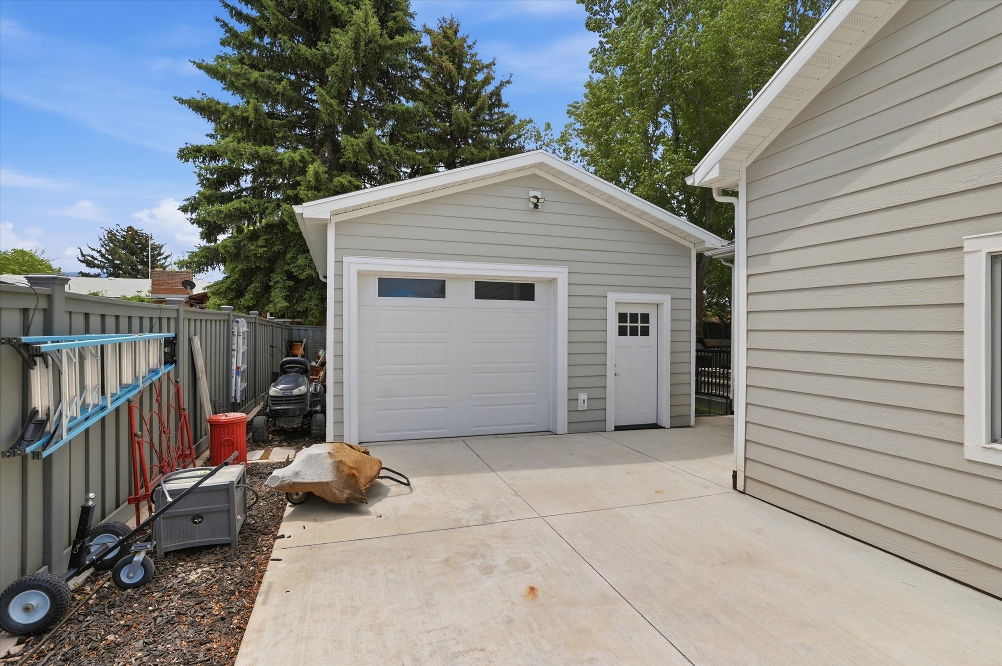 Detached single-car garage featuring light gray siding, a white garage door with upper windows, and a side entry door with lites