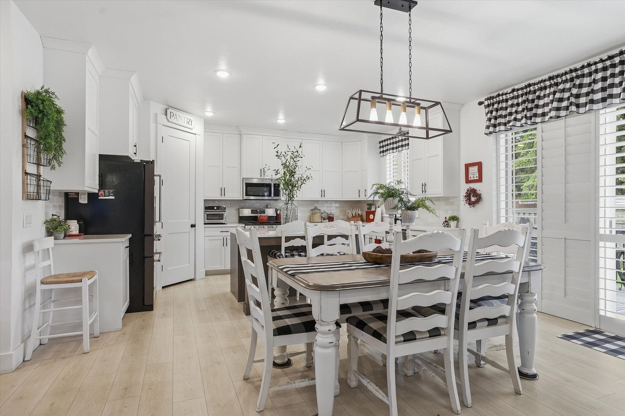 Bright kitchen featuring white cabinetry, light wood-finish flooring, a pantry door, a central island, and white plantation shutters