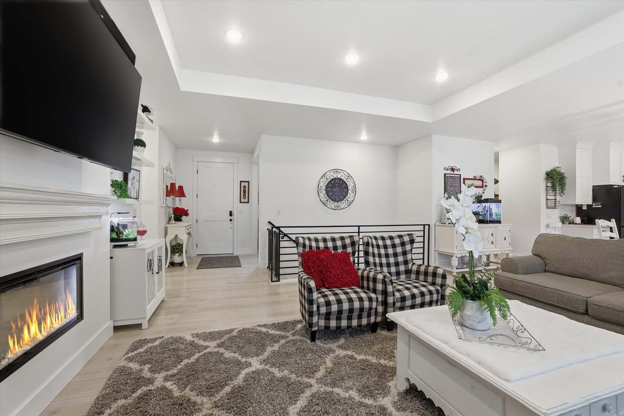 Open living space featuring a built-in electric fireplace with a white mantel, light wood-finish flooring, recessed lighting, and a partial view of a kitchen area