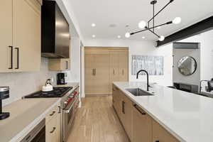 Contemporary kitchen featuring light wood-finish cabinetry, a large center island with an undermount sink and matte black faucet, integrated stainless steel appliances, and wood-finish flooring