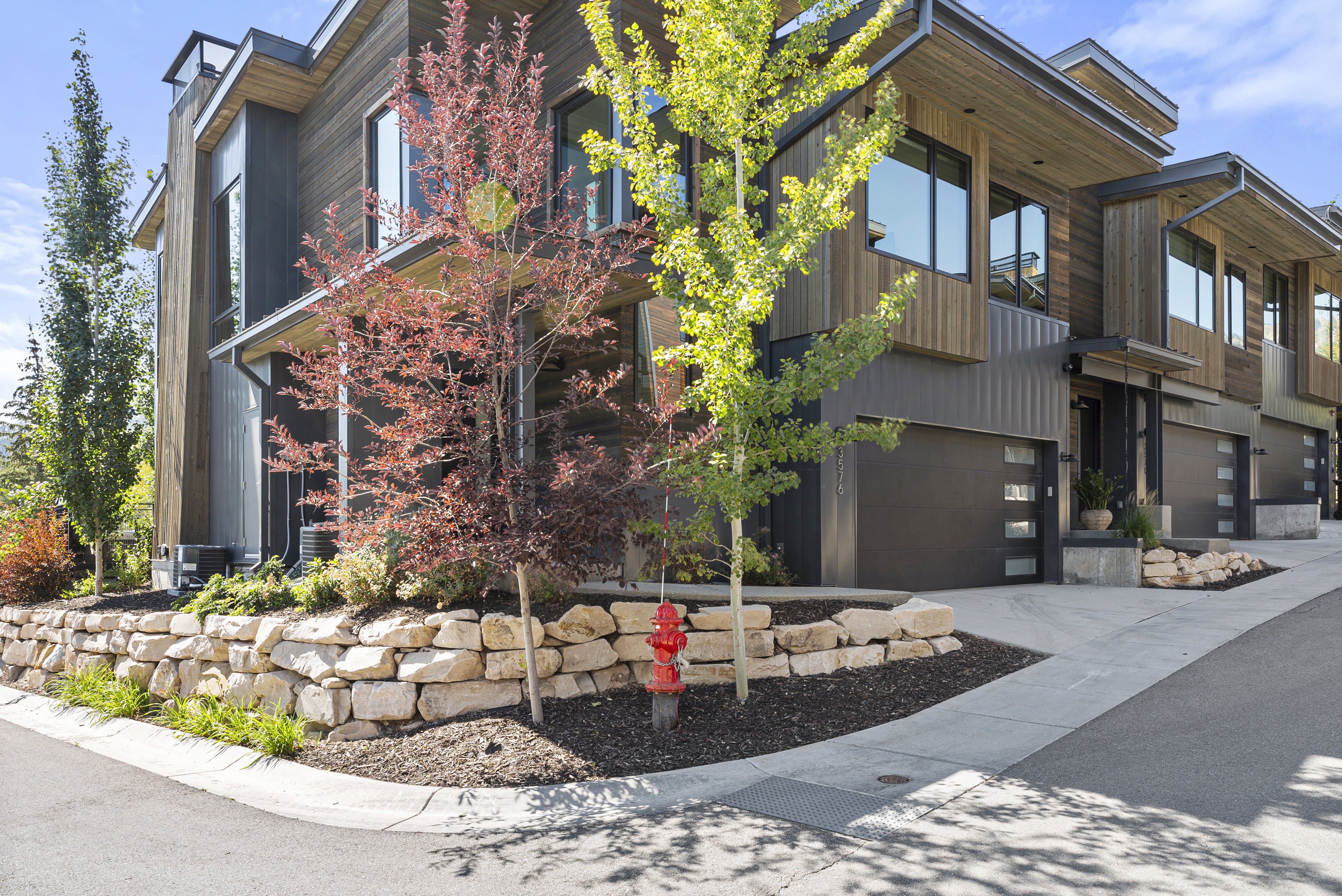 Modern multi-level townhome featuring dark wood-look siding, corrugated metal accents, and a stone retaining wall