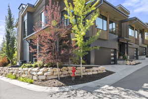 Modern multi-level townhome featuring dark wood-look siding, corrugated metal accents, and a stone retaining wall