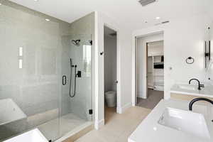 Spacious bathroom featuring a glass-enclosed shower with matte black fixtures, dual vanities with white countertops, and a separate water closet