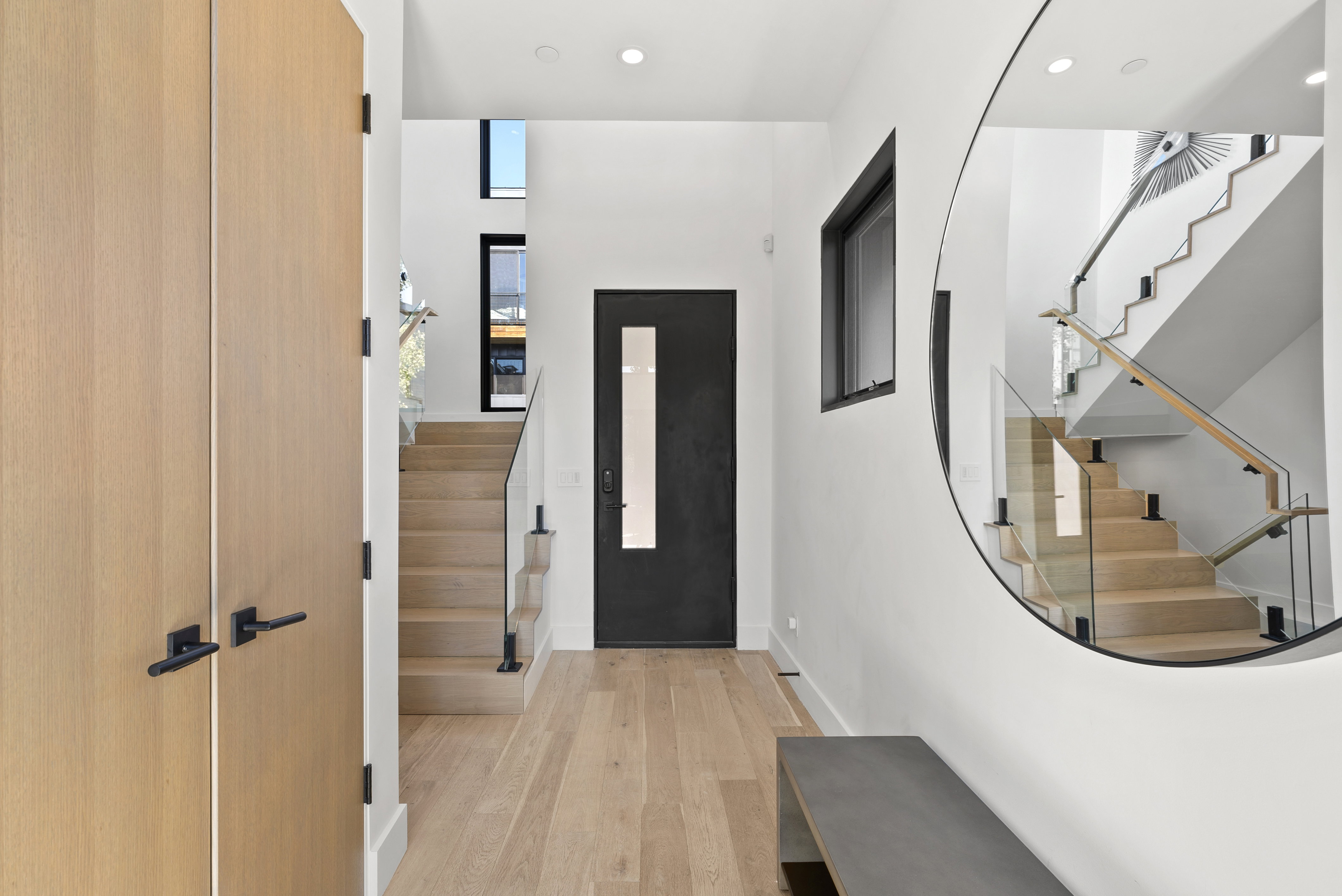 Entryway featuring wood-finish flooring, a contemporary staircase with glass railings and wood handrails, and a solid core entry door with vertical glass insert.
