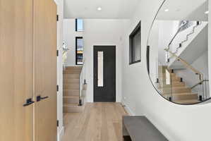 Entryway featuring wood-finish flooring, a contemporary staircase with glass railings and wood handrails, and a solid core entry door with vertical glass insert.