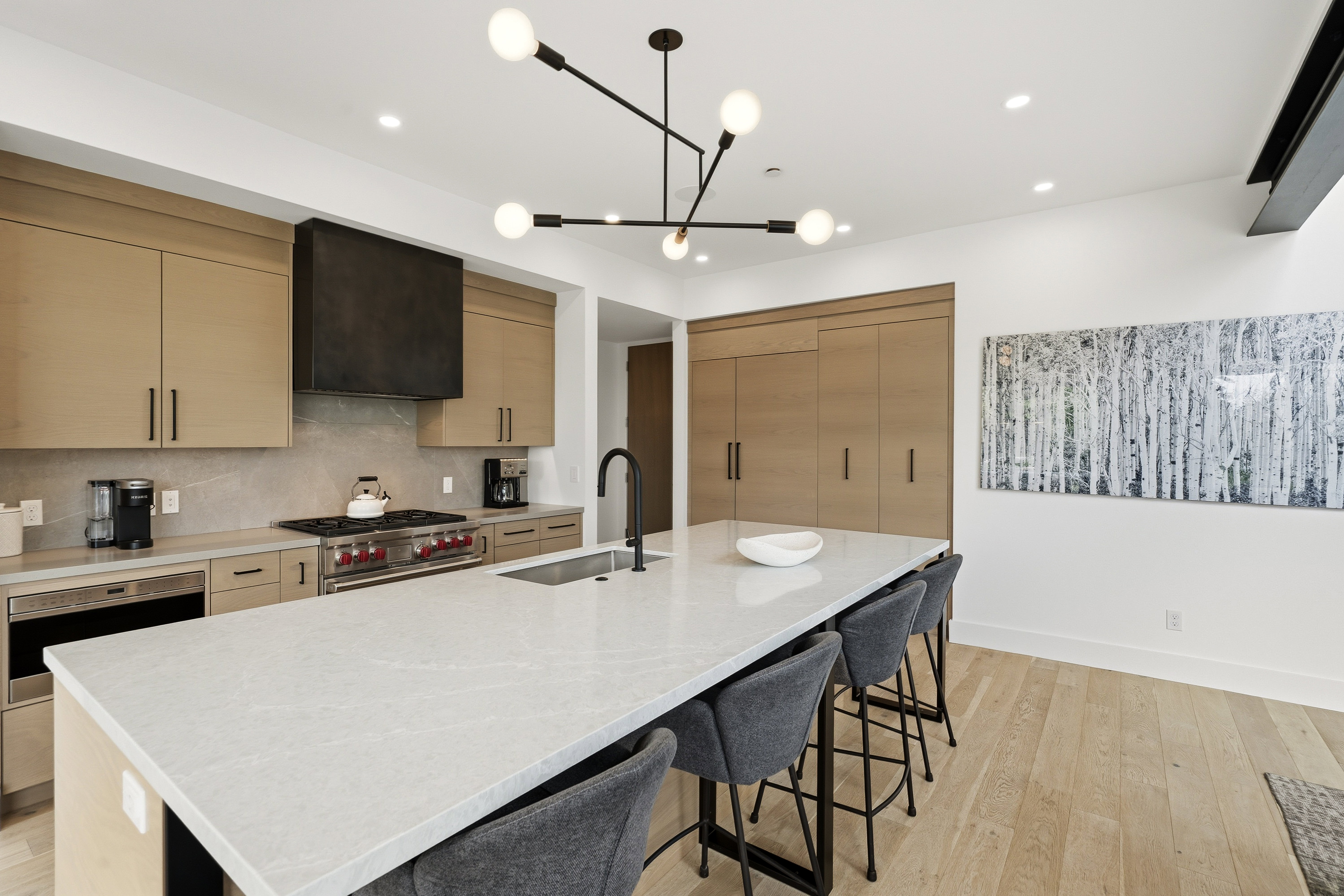 Gourmet kitchen featuring a substantial island with seating, a professional-grade range, custom light wood-finish cabinetry, a large built-in refrigerator, and light wood-finish flooring