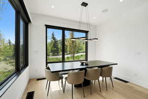 Dining area featuring large black-framed windows, a contemporary linear chandelier, recessed lighting, and wood-finish flooring