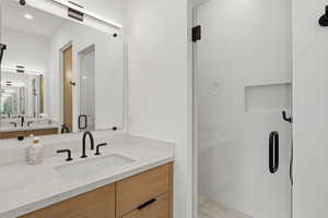 Contemporary bathroom featuring a light wood-finish vanity with drawer storage, a white countertop with an integrated rectangular sink, and matte black fixtures