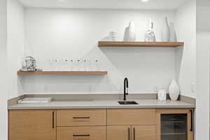 Modern wet bar featuring natural wood-finish cabinetry, a light-toned countertop, and a built-in beverage cooler